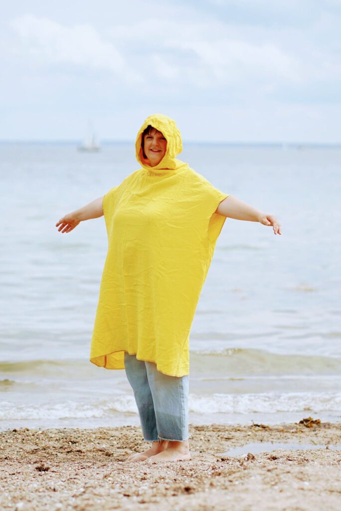 Tine steht am Ostseestrand und trägt den Surfponcho über einer hellen Jeans. Sie streckt die Arme aus, sodass die Form des Ponchos gut zu erkennen ist.
